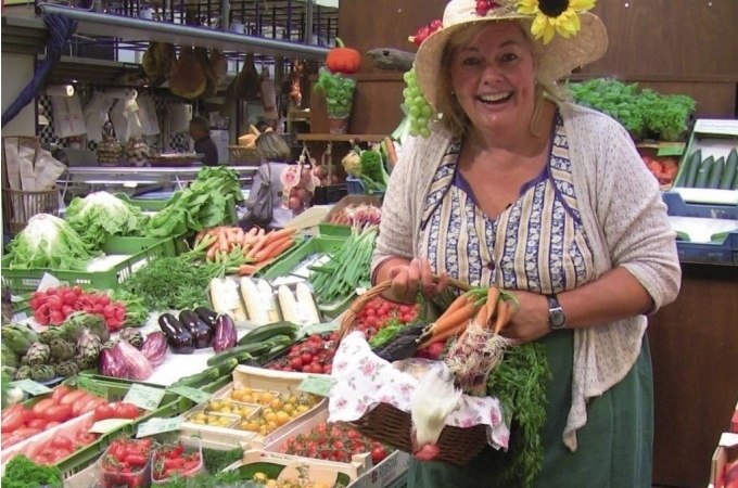 Frau mit Sonnenblumenhut in einer Markthalle, lächelnd, umgeben von frischem Gemüse und Obst. Sie hält einen Korb mit Karotten und Kräutern., © Stuttgart Marketing GmbH Frau mit Sonnenblumenhut in einer Markthalle, lächelnd, umgeben von frischem Gemüse und Obst. Sie hält einen Korb mit Karotten und Kräutern., © Stuttgart Marketing GmbH