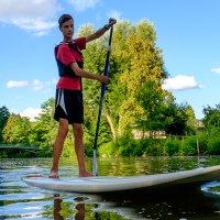 Eine Person steht auf einem Stand Up Paddle Board auf einem Fluss, umgeben von grüner Natur und blauem Himmel., © WTM GmbH Waiblingen