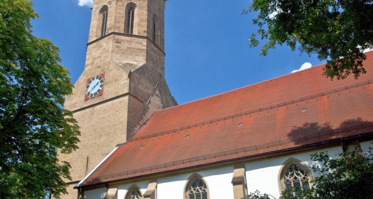 Kirche mit hohem Turm und roten Dachziegeln, umgeben von Bäumen. Der Himmel ist blau mit wenigen Wolken., © Waiblingen - Stuttgart-Marketing GmbH Kirche mit hohem Turm und roten Dachziegeln, umgeben von Bäumen. Der Himmel ist blau mit wenigen Wolken., © Waiblingen - Stuttgart-Marketing GmbH
