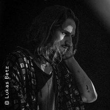 Ein DJ mit langen Haaren und gemustertem Hemd legt in einer dunklen Umgebung auf. Die Aufnahme ist in Schwarz-Wei&szlig; gehalten., &copy; links im Bild