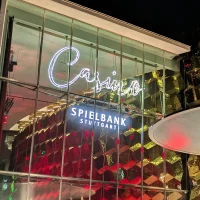 Die Spielbank Stuttgart bei Nacht: beleuchtete Glasfassade, goldene Kubusstruktur und markantes wei&szlig;es Schirmdach., &copy; SMG
