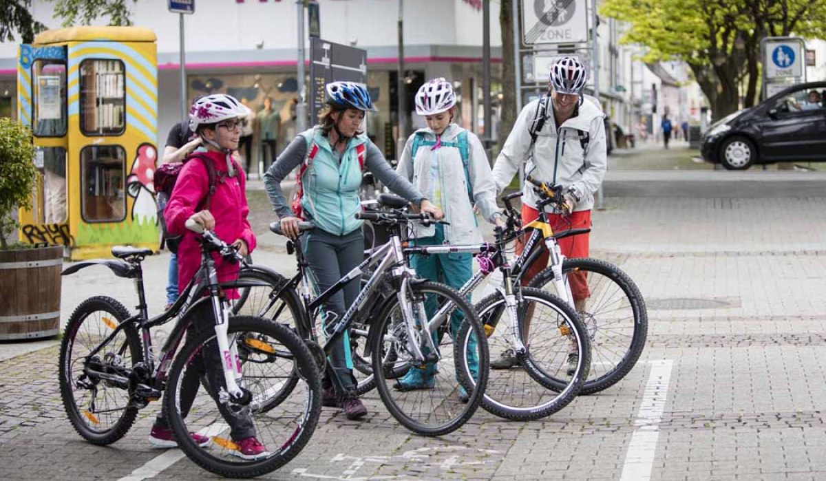 Vier Personen mit Fahrrädern und Helmen stehen in einer Fußgängerzone. Im Hintergrund ist eine bemalte Telefonzelle zu sehen., © Schwäbische Alb Tourismusverband e.V. Vier Personen mit Fahrrädern und Helmen stehen in einer Fußgängerzone. Im Hintergrund ist eine bemalte Telefonzelle zu sehen., © Schwäbische Alb Tourismusverband e.V.