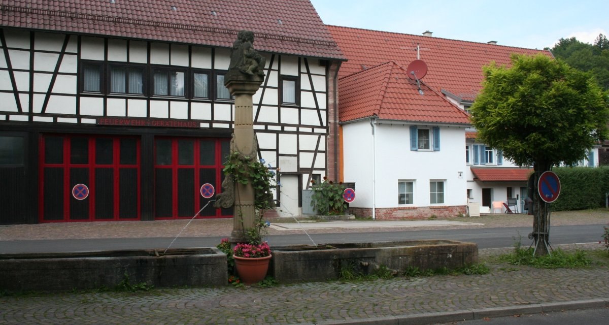 Fachwerkhaus mit rotem Dach, Feuerwehr-Gerätehaus. Im Vordergrund ein Brunnen mit Blumen. Parkverbotsschilder und ein Baum sind sichtbar., © Natur.Nah. Schönbuch & Heckengäu Fachwerkhaus mit rotem Dach, Feuerwehr-Gerätehaus. Im Vordergrund ein Brunnen mit Blumen. Parkverbotsschilder und ein Baum sind sichtbar., © Natur.Nah. Schönbuch & Heckengäu