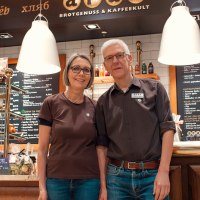 Zwei Personen stehen lächelnd vor einem Café namens 'aran', das Brotgenuss und Kaffeekultur anbietet., © Cafe aran