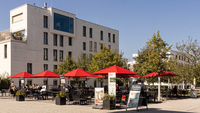 Moderne Wohngebäude in Stuttgart Killesberghöhe, mit roten Sonnenschirmen und Menschen auf einem Platz bei sonnigem Wetter., © Stuttgart-Marketing GmbH, Sarah Schmid Moderne Wohngebäude in Stuttgart Killesberghöhe, mit roten Sonnenschirmen und Menschen auf einem Platz bei sonnigem Wetter., © Stuttgart-Marketing GmbH, Sarah Schmid