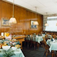 Fr&uuml;hst&uuml;cksraum mit gedeckten Tischen, Holzst&uuml;hlen und einem Buffet mit Br&ouml;tchen, Obst und Saft. Holzw&auml;nde und h&auml;ngende Lampen schaffen eine gem&uuml;tliche Atmosph&auml;re., &copy; Hotel Find