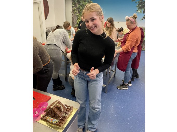 Eine Frau in schwarzem Pullover und Jeans präsentiert stolz ein Lebkuchenhaus in einer Küche mit anderen Teilnehmern im Hintergrund., © Alfred Ritter GmbH & Co. KG | Waldenbuch Eine Frau in schwarzem Pullover und Jeans präsentiert stolz ein Lebkuchenhaus in einer Küche mit anderen Teilnehmern im Hintergrund., © Alfred Ritter GmbH & Co. KG | Waldenbuch