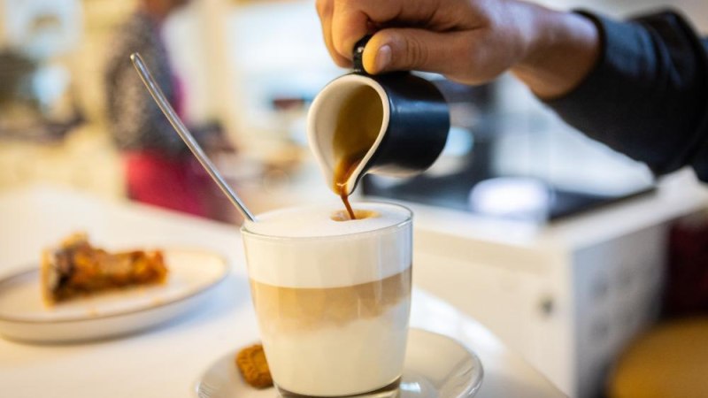Eine Hand gie&szlig;t Espresso in ein Glas mit Milchschaum. Im Hintergrund steht ein Teller mit Kuchen auf einem Tisch., &copy; Ludwigsburg Museum