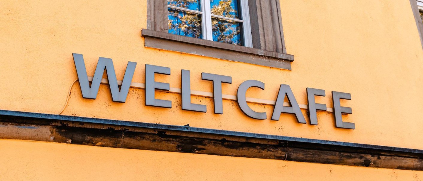 Der Schriftzug 'Weltcafé' prangt in großen Buchstaben an einer gelben Wand, unterhalb eines Fensters mit blauem Rahmen., © Stuttgart-Marketing GmbH, Sarah Schmid Der Schriftzug 'Weltcafé' prangt in großen Buchstaben an einer gelben Wand, unterhalb eines Fensters mit blauem Rahmen., © Stuttgart-Marketing GmbH, Sarah Schmid