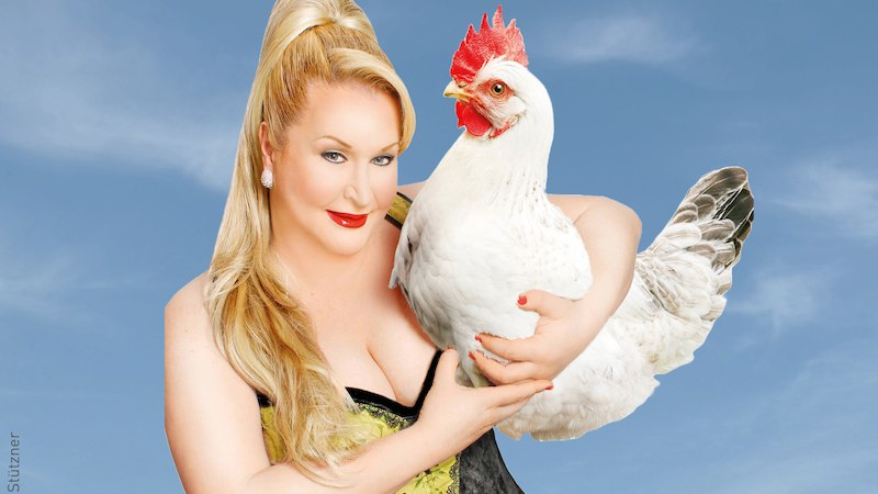 Eine Person mit blonden Haaren h&auml;lt ein wei&szlig;es Huhn vor einem blauen Himmel. Sie tr&auml;gt ein elegantes Outfit und l&auml;chelt in die Kamera., &copy; Stadt Kornwestheim Kulturmanagement