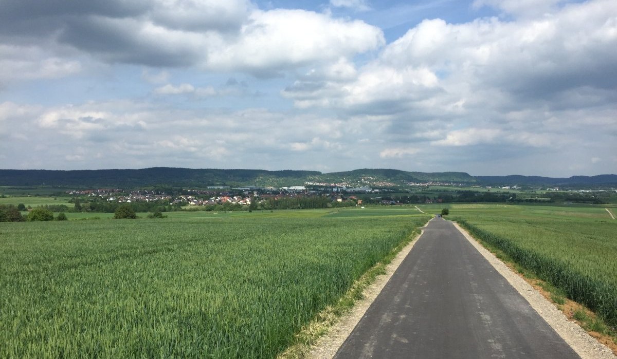 Ein asphaltierter Radweg f&uuml;hrt durch gr&uuml;ne Felder in Richtung des Dorfes G&uuml;ltstein. Der Himmel ist bew&ouml;lkt, und die Landschaft wirkt friedlich., &copy; www.pro-cycl.de