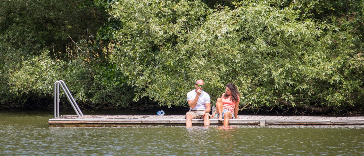 Zwei Personen sitzen auf einem Steg am Wasser, umgeben von üppigem Grün. Sie genießen die Natur im Naherholungsgebiet Bürgerseen Kirchheim unter Teck., © Stadt Kirchheim unter Teck