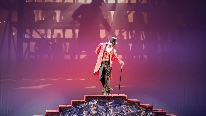 Ein Plakat f&uuml;r die Kinovorf&uuml;hrung von 'The Greatest Showman' mit live getanzten Filmszenen. Ein Mann in rotem Frack h&auml;lt einen Zylinderhut., &copy; Stadthalle Leonberg