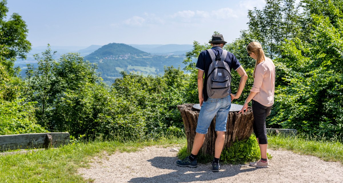 Zwei Personen betrachten die Aussicht vom Hohenstaufen auf den Rechberg. Der bewaldete Hügel ist von grünen Bäumen umgeben., © TMBW, Gregor Lengler Zwei Personen betrachten die Aussicht vom Hohenstaufen auf den Rechberg. Der bewaldete Hügel ist von grünen Bäumen umgeben., © TMBW, Gregor Lengler