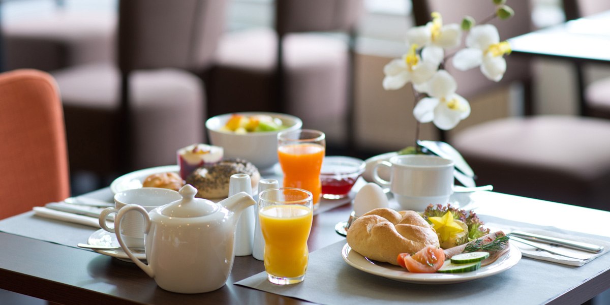 Ein Fr&uuml;hst&uuml;ckstisch mit Br&ouml;tchen, Orangensaft, Tee, Obst, Ei und einer Orchidee als Dekoration., &copy; ACHAT Hotels Deutschland
