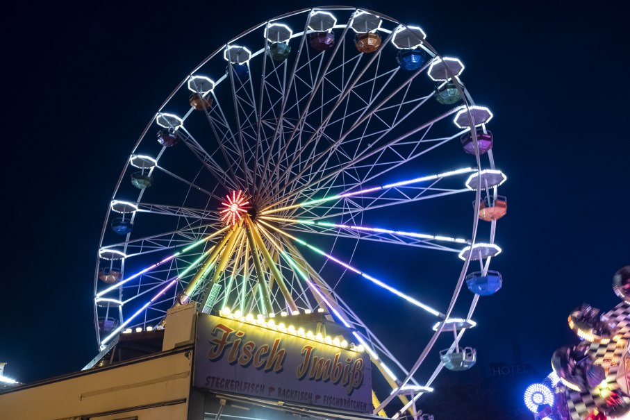 Ein beleuchtetes Riesenrad bei Nacht auf einem Jahrmarkt, mit einem Fisch-Imbiss im Vordergrund., © Torsten Wenzler Ein beleuchtetes Riesenrad bei Nacht auf einem Jahrmarkt, mit einem Fisch-Imbiss im Vordergrund., © Torsten Wenzler