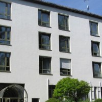 Mehrstöckiges Gebäude mit weißen Wänden und zahlreichen Fenstern, umgeben von Bäumen und Sträuchern., © Christkönigshaus