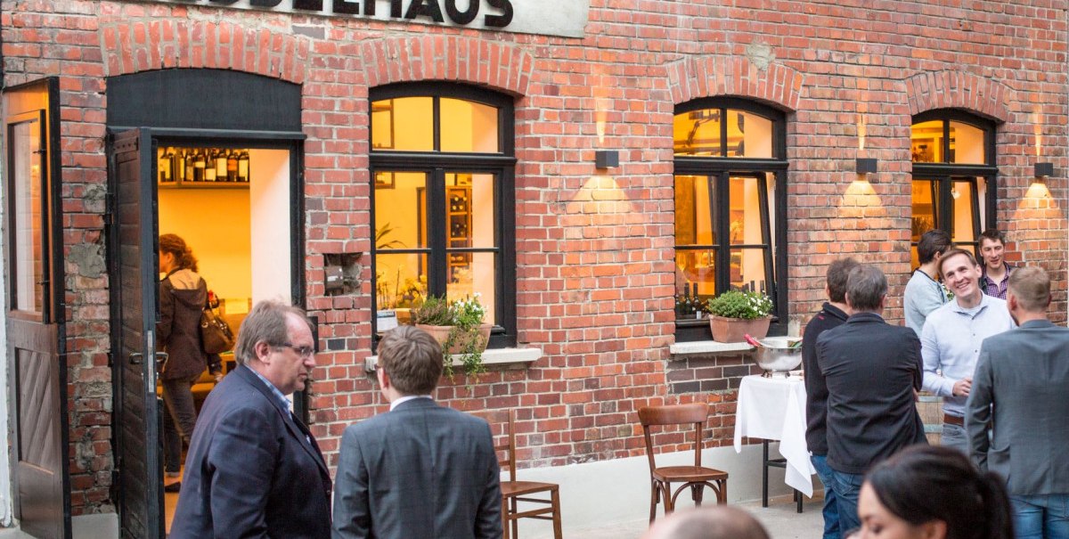 Menschen unterhalten sich vor einem Backsteingeb&auml;ude mit der Aufschrift 'Kesselhaus'. Es herrscht eine gesellige Atmosph&auml;re.