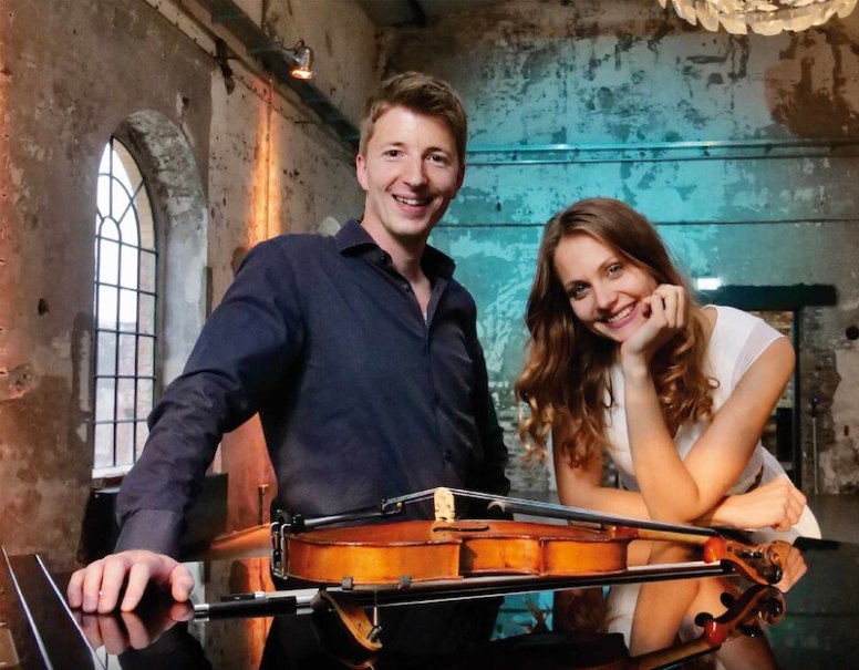 Ein Mann und eine Frau lächeln in einem rustikalen Raum. Eine Geige liegt auf einem Tisch vor ihnen. Der Raum hat große Fenster und eine abgenutzte Wand., © Schönblick gemeinnützige GmbH