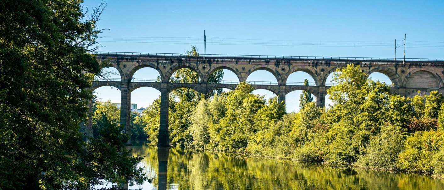 Das Bietigheim-Bissingen Viadukt erstreckt sich über einen Fluss, umgeben von üppigem Grün. Der blaue Himmel spiegelt sich im Wasser wider., © Stuttgart-Marketing GmbH, Sarah Schmid Das Bietigheim-Bissingen Viadukt erstreckt sich über einen Fluss, umgeben von üppigem Grün. Der blaue Himmel spiegelt sich im Wasser wider., © Stuttgart-Marketing GmbH, Sarah Schmid