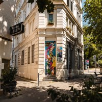 Eine Straßenecke mit einem Pub-Schild, bunter Wandkunst und Café-Tischen unter einem Sonnenschirm., © SMG Stuttgart Marketing GmbH - Sarah Schmid