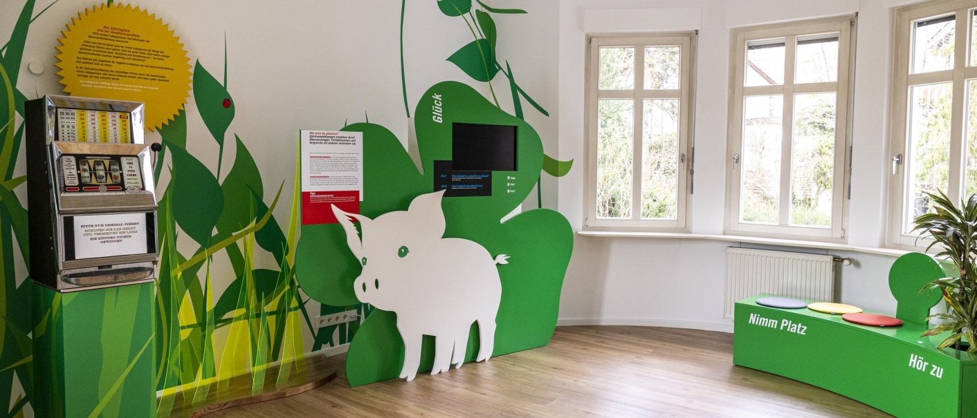 Ein Ausstellungsraum mit einem Spielautomaten, grüner Dekoration und Sitzgelegenheiten. Ein Schwein als Dekorationselement ist sichtbar., © Stuttgart-Marketing GmbH, Sarah Schmid Ein Ausstellungsraum mit einem Spielautomaten, grüner Dekoration und Sitzgelegenheiten. Ein Schwein als Dekorationselement ist sichtbar., © Stuttgart-Marketing GmbH, Sarah Schmid