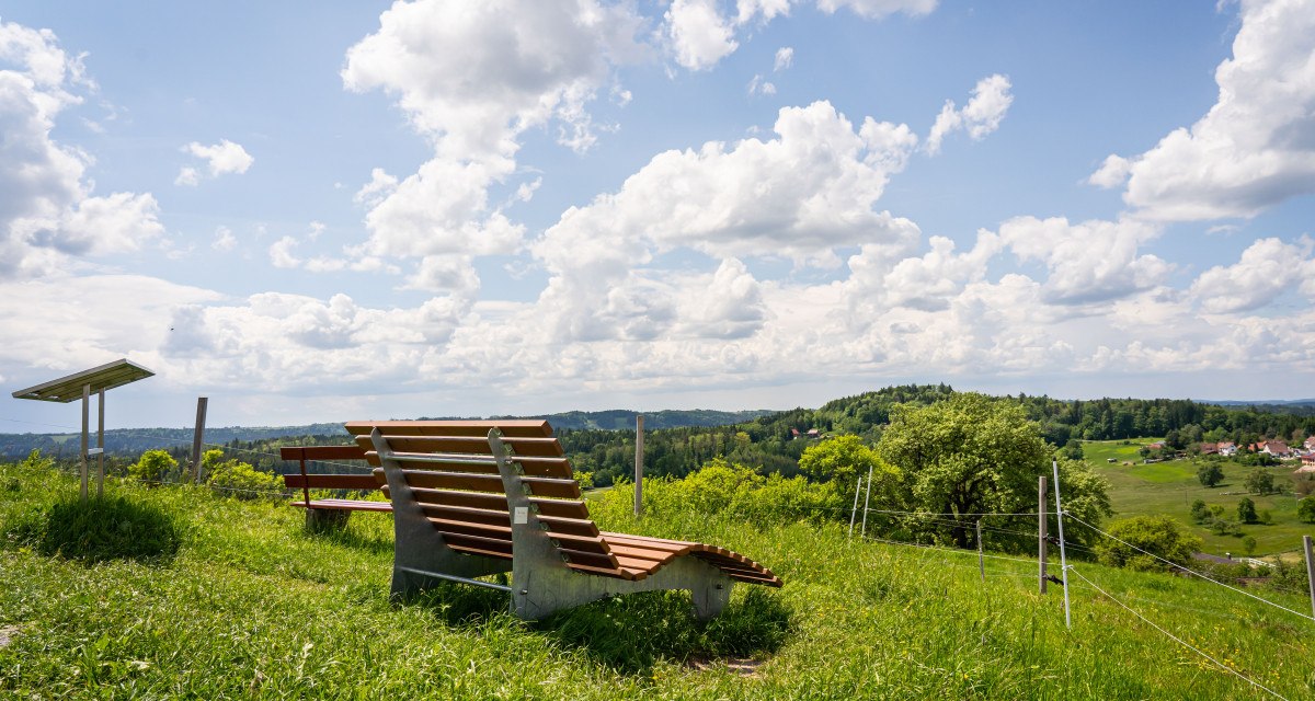 Ruheliege auf einer grünen Wiese am Aussichtspunkt "Hohe Tanne" mit Blick auf eine hügelige Landschaft und einen bewölkten Himmel., © agentur arcos/Niki Eilers