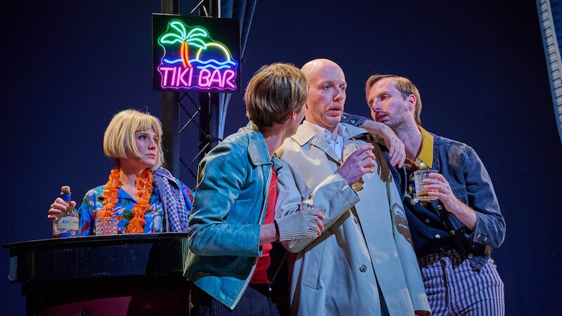 Vier Personen in einer Bar-Szene, eine Frau mit blonder Per&uuml;cke, zwei M&auml;nner in Gespr&auml;ch, Neon-Tiki-Bar-Schild im Hintergrund., &copy; Kulturb&uuml;ro Schw&auml;bisch Gm&uuml;nd