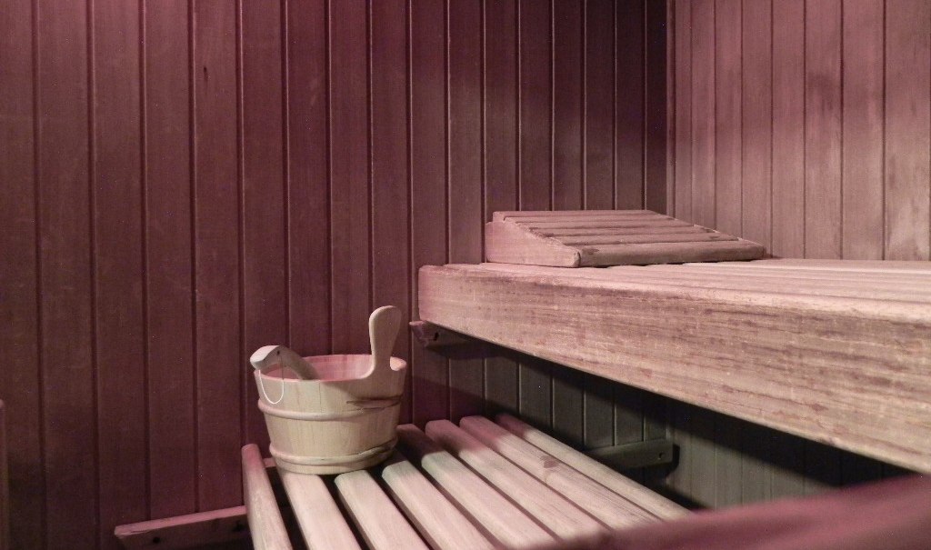 Innenansicht einer Sauna mit Holzbänken, einem Holzeimer und einem Holzrückenlehner. Die Wände sind aus Holzpaneelen., © Hotel Gloria GmbH Restaurant Möhringer Hexle