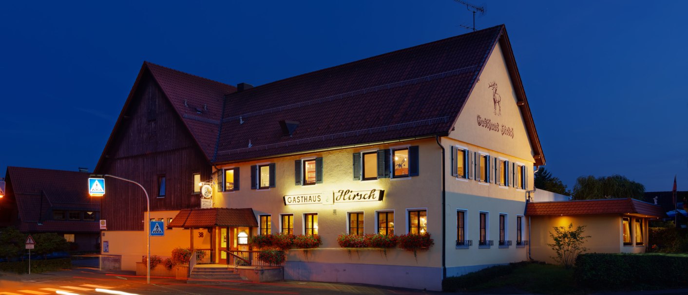 Das Gasthaus Hirsch bei Nacht, beleuchtet mit gelber Fassade und roten Dachziegeln. Ein Zebrastreifen und Straßenschilder sind im Vordergrund sichtbar., © Dieter Schurr, Gasthaus Hirsch