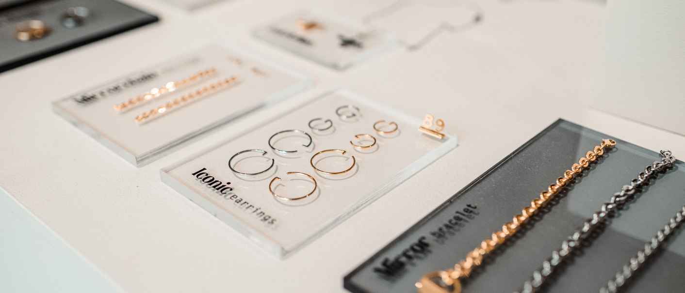 Nahaufnahme von Schmuck auf einem Tisch, darunter goldene und silberne Ohrringe und Armbänder auf schwarzen und weißen Karten., © Goldmarlen