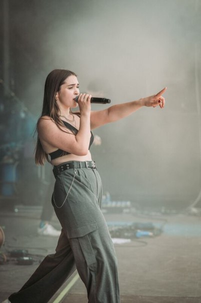 Eine Sängerin performt auf der Bühne. Sie trägt ein schwarzes Top und graue Hosen, hält ein Mikrofon und zeigt mit dem Finger nach vorne., © Interessengemeinschaft Kultur Sindelfingen / Böblingen e.V. Eine Sängerin performt auf der Bühne. Sie trägt ein schwarzes Top und graue Hosen, hält ein Mikrofon und zeigt mit dem Finger nach vorne., © Interessengemeinschaft Kultur Sindelfingen / Böblingen e.V.