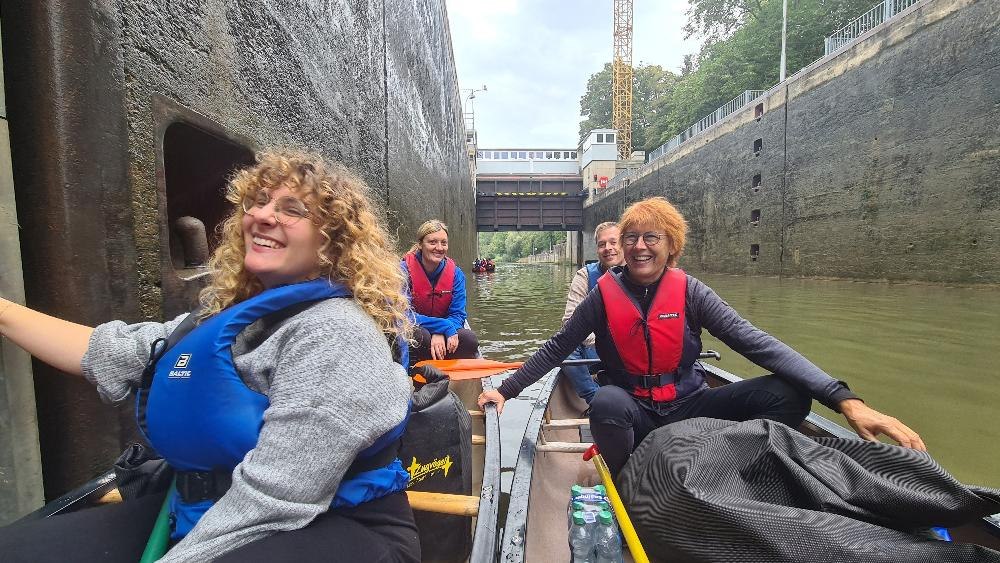 Eine fr&ouml;hliche Gruppe von Menschen in einem Kanu passiert eine Schleuse auf dem Neckar. Sie tragen Schwimmwesten und genie&szlig;en die Kanutour., &copy; Die Zugv&ouml;gel - Kanu-Tours und mehr