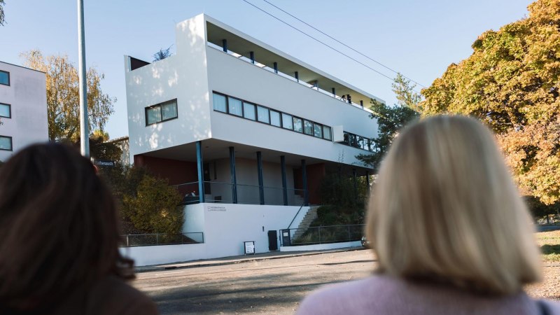 Zwei Personen betrachten das Haus Le Corbusier in der Weißenhofsiedlung. Modernes Gebäude mit klaren Linien, umgeben von herbstlichen Bäumen., © Stuttgart-Marketing GmbH, wpsteinheisser Zwei Personen betrachten das Haus Le Corbusier in der Weißenhofsiedlung. Modernes Gebäude mit klaren Linien, umgeben von herbstlichen Bäumen., © Stuttgart-Marketing GmbH, wpsteinheisser