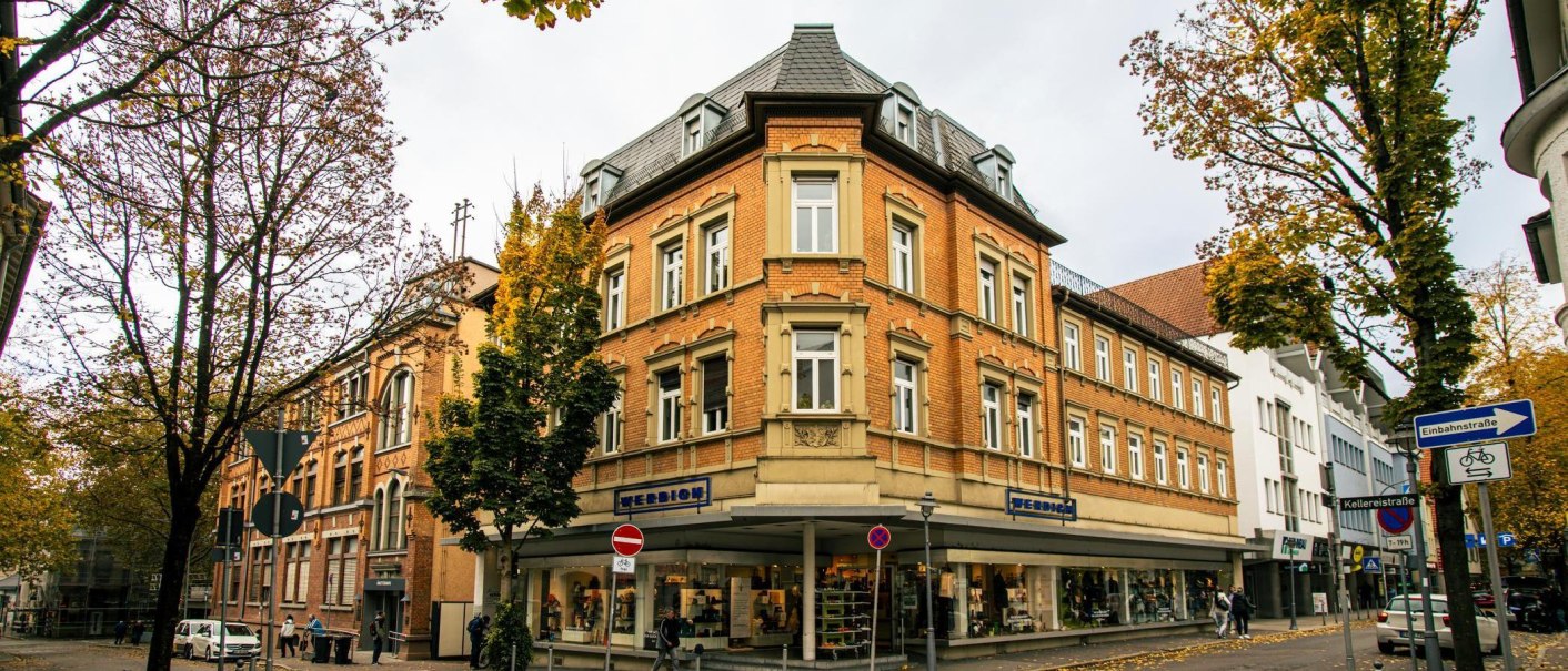 Historische Gebäude in der Innenstadt von Göppingen, umgeben von herbstlichen Bäumen. Ein Geschäft mit Schaufenstern und Straßenschilder sind sichtbar., © Stuttgart-Marketing GmbH, Sarah Schmid Historische Gebäude in der Innenstadt von Göppingen, umgeben von herbstlichen Bäumen. Ein Geschäft mit Schaufenstern und Straßenschilder sind sichtbar., © Stuttgart-Marketing GmbH, Sarah Schmid