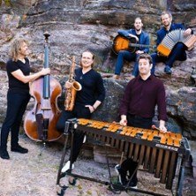 Eine Musikgruppe posiert mit Instrumenten wie Kontrabass, Saxophon, Gitarre, Akkordeon und Vibraphon vor einer Felswand., &copy; links im Bild