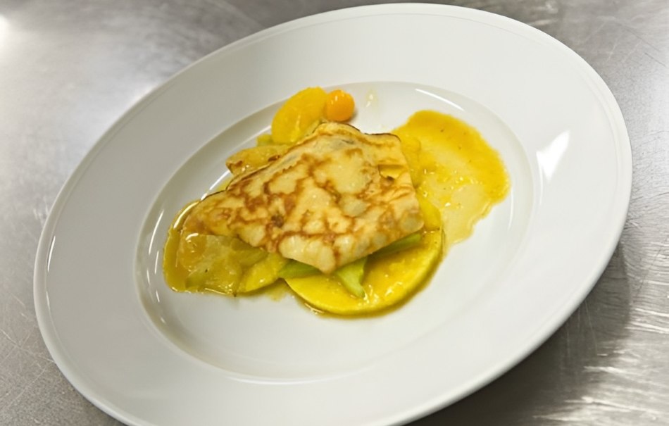 Ein Crêpe mit Orangensauce und Früchten auf einem weißen Teller, präsentiert auf einer Metalloberfläche., © Hotel Neuwirtshaus