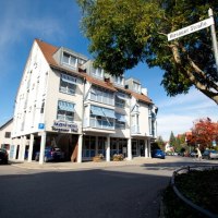 Das AKZENT Hotel Torgauer Hof an einer Straßenecke mit blauen Markisen und einem Baum im Vordergrund., © AKZENT Hotel Torgauer Hof