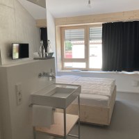 Modernes Zimmer mit Holzrahmenbett, Waschbecken, Fernseher und großem Fenster mit Vorhängen. Schlichte, minimalistische Einrichtung., © Remstal Tourismus e.V.
