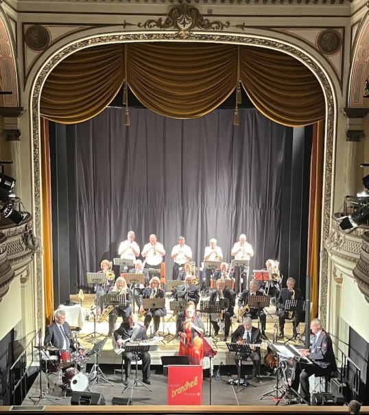Die Brandhei&szlig; Bigband spielt auf einer eleganten Theaterb&uuml;hne. Die Musiker sind in formeller Kleidung und die B&uuml;hne ist mit goldenen Vorh&auml;ngen geschm&uuml;ckt., &copy; Touristik Bad Wildbad GmbH