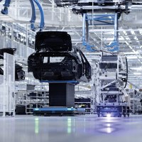 Eine moderne Fabrikhalle zeigt die Fahrzeugmontage mit Robotern und Fahrzeugkarosserien. Die Umgebung ist hell und technologisch fortschrittlich., &copy; Mercedes-Benz AG