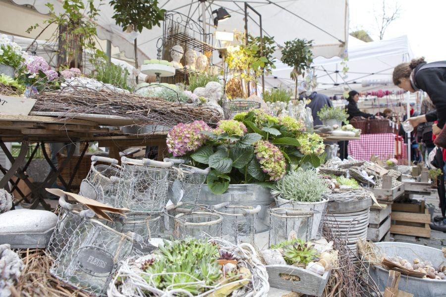 Ein Marktstand in Esslingen mit Blumen, Pflanzen und dekorativen Gegenständen. Menschen stöbern durch die Auslagen unter weißen Pavillons., © EST