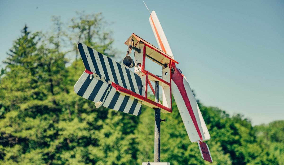 Ein buntes Holzflugzeugmodell auf einem Pfosten vor einem bewaldeten Hintergrund unter klarem Himmel., © Tourismus Ostalb