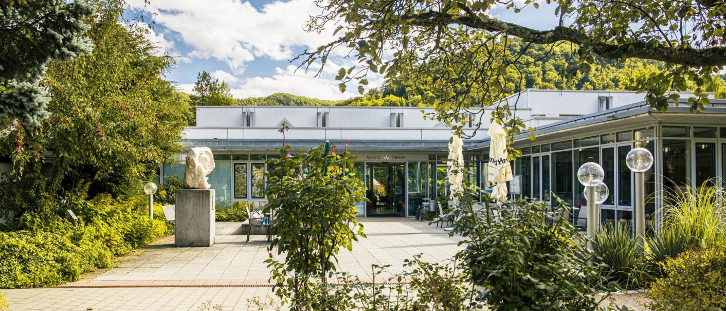 Eingang der Vinzenz Therme in Bad Ditzenbach, umgeben von Bäumen und Pflanzen. Moderne Architektur mit Glasfronten und Skulpturen im Vordergrund., © Stuttgart-Marketing GmbH, Sarah Schmid Eingang der Vinzenz Therme in Bad Ditzenbach, umgeben von Bäumen und Pflanzen. Moderne Architektur mit Glasfronten und Skulpturen im Vordergrund., © Stuttgart-Marketing GmbH, Sarah Schmid