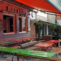 Au&szlig;enbereich eines Caf&eacute;s namens Mos Eisley mit bunten Tischen und B&auml;nken. Daneben ein S- und U-Bahn-Schild am Roteb&uuml;hlplatz Stadtmitte., &copy; SMG