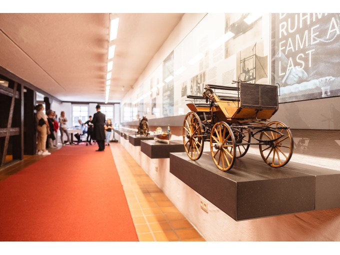 Ein historisches Fahrzeugmodell in einem Museum. Besucher betrachten die Ausstellung entlang eines roten Teppichs., &copy; Eigenbetrieb Tourismus und Citymanagement Schorndorf