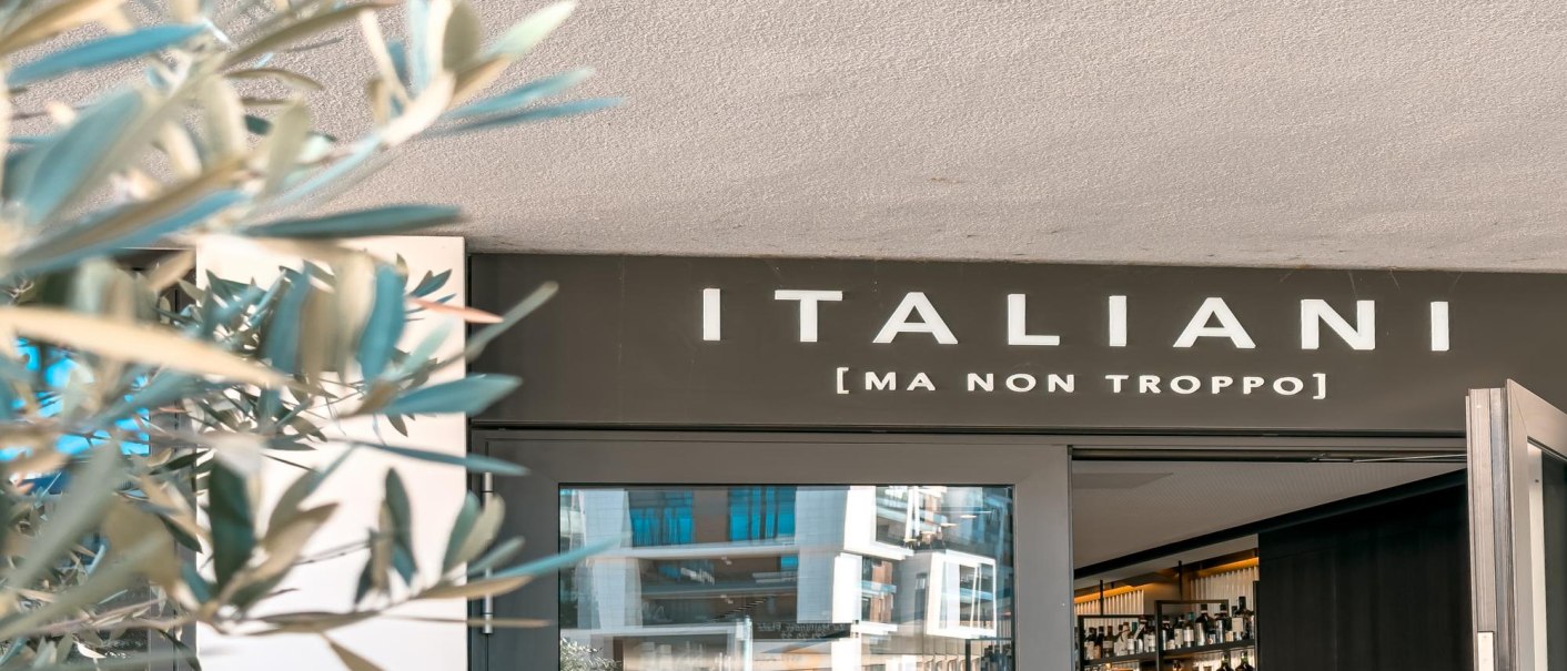 Eingang eines Restaurants mit dem Schild 'ITALIANI [MA NON TROPPO]'. Im Vordergrund sind unscharfe Pflanzen zu sehen., © SMG Stuttgart Marketing GmbH - Sarah Schmid