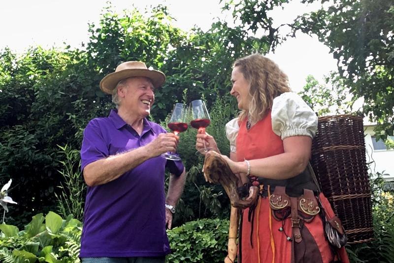 Ein Mann und eine Frau sto&szlig;en im Garten mit Rotweingl&auml;sern an. Die Frau tr&auml;gt ein traditionelles Kost&uuml;m und einen Wanderstock., &copy; Foto: G&uuml;nther Schuster