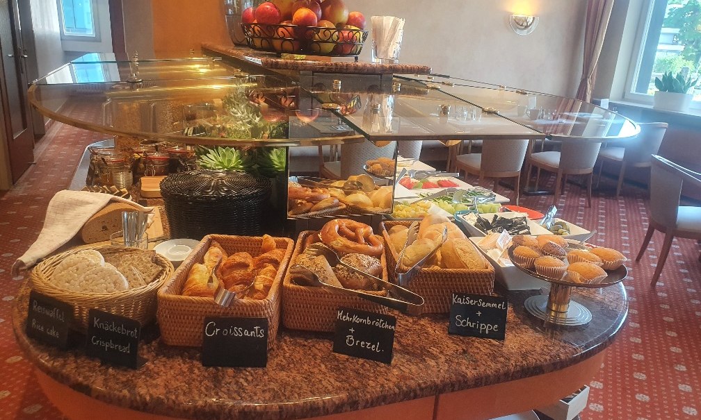 Ein reichhaltiges Frühstücksbüffet mit Brotkörben, Croissants, Brezeln, Obst und Muffins in einem eleganten Raum., © PLAZA INN Rieker Stuttgart Hauptbahnhof Ein reichhaltiges Frühstücksbüffet mit Brotkörben, Croissants, Brezeln, Obst und Muffins in einem eleganten Raum., © PLAZA INN Rieker Stuttgart Hauptbahnhof