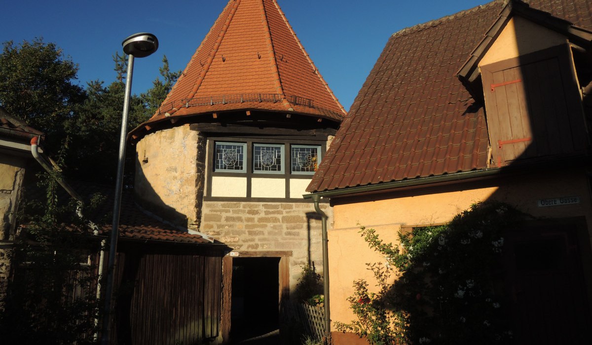 Historisches Gebäude mit rundem Turm und Fachwerkfenstern, umgeben von Häusern mit roten Dächern und blühenden Pflanzen., © Land der 1000 Hügel - Kraichgau-Stromberg Historisches Gebäude mit rundem Turm und Fachwerkfenstern, umgeben von Häusern mit roten Dächern und blühenden Pflanzen., © Land der 1000 Hügel - Kraichgau-Stromberg